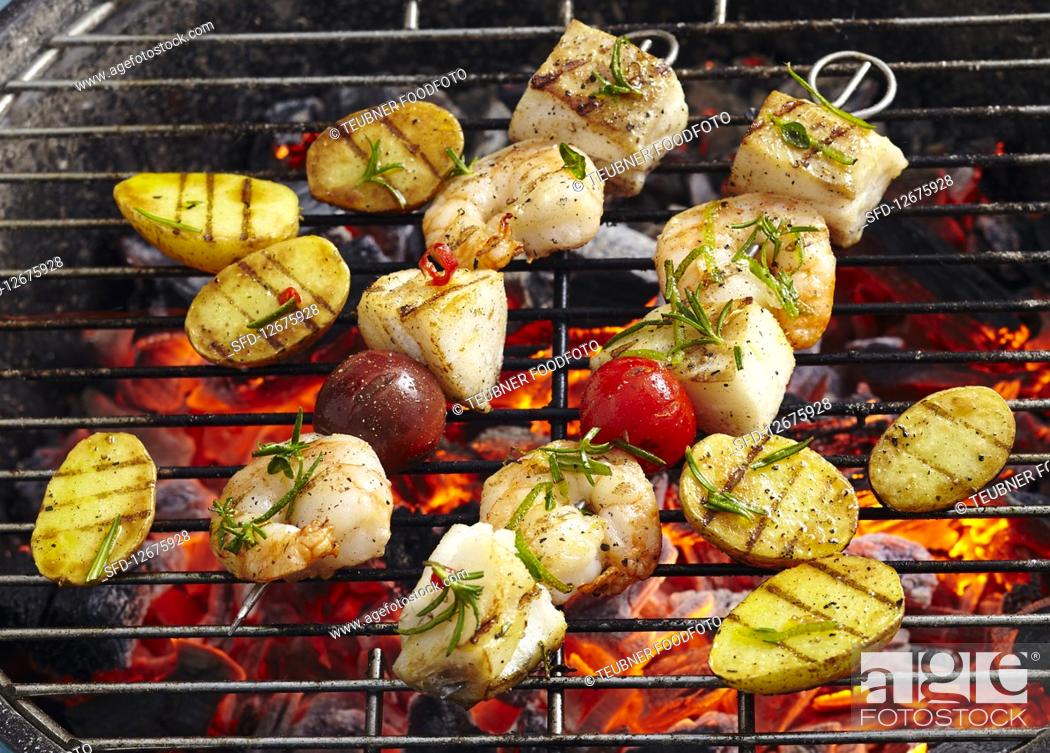 Imagen: Cod and prawn skewers with grilled potatoes on a coal-fired grill.