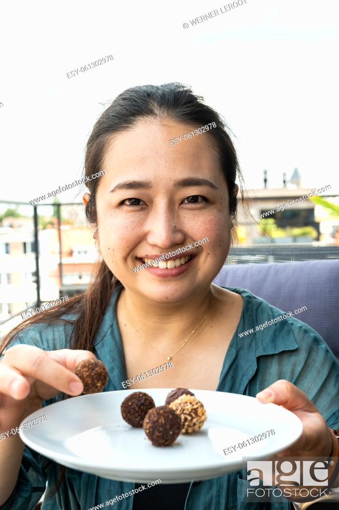 Imagen: Portrait of a 32 year old Japanese woman holding a plate of round chocolates, Belgium.