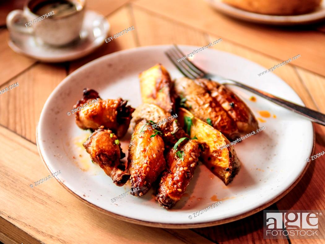 Stock Photo: Tasty roasted chicken wings and roasted potatoes. Authentic shot of plate with roasted chicken wings and roasted potatoes on rustic wooden tabletop.