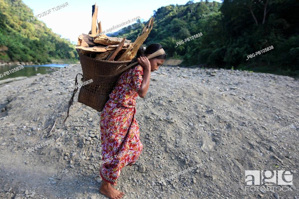 Stock Photo: An ethnic Marma woman carries basket of firewood on her back at the bank of Sangu river Bandarban, Bangladesh December 2009.