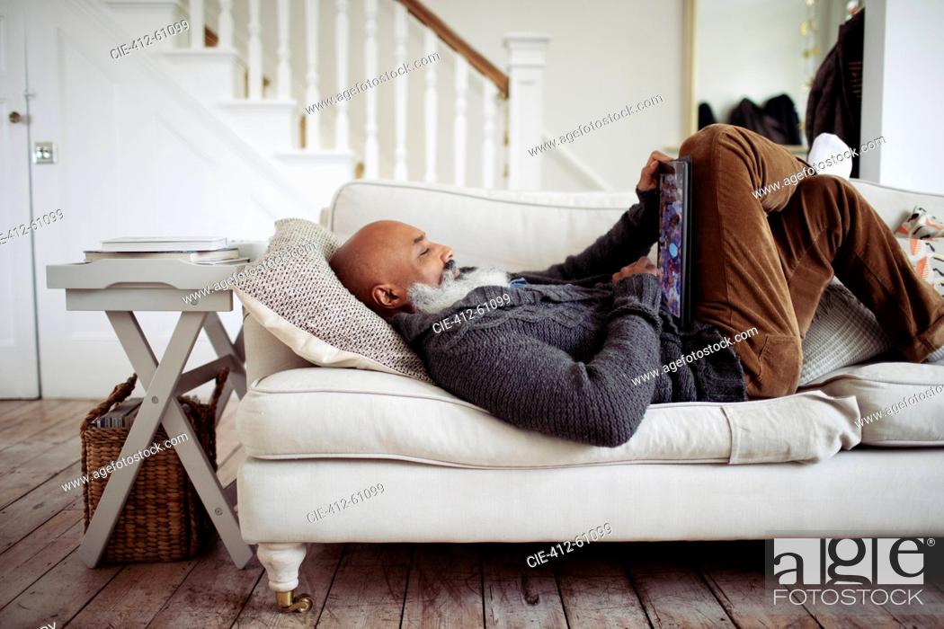 Stock Photo: Mature man relaxing on living room sofa with digital tablet.