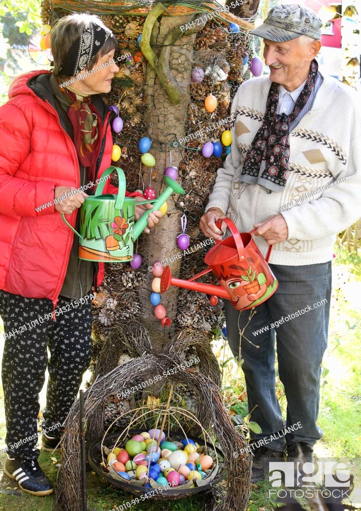 Stock Photo: 02 October 2021, Saxony, Leipzig: The couple Ingrid and Fritz Hundt are standing in ""their"" Hundt park by a tree trunk decorated with Easter eggs from the.