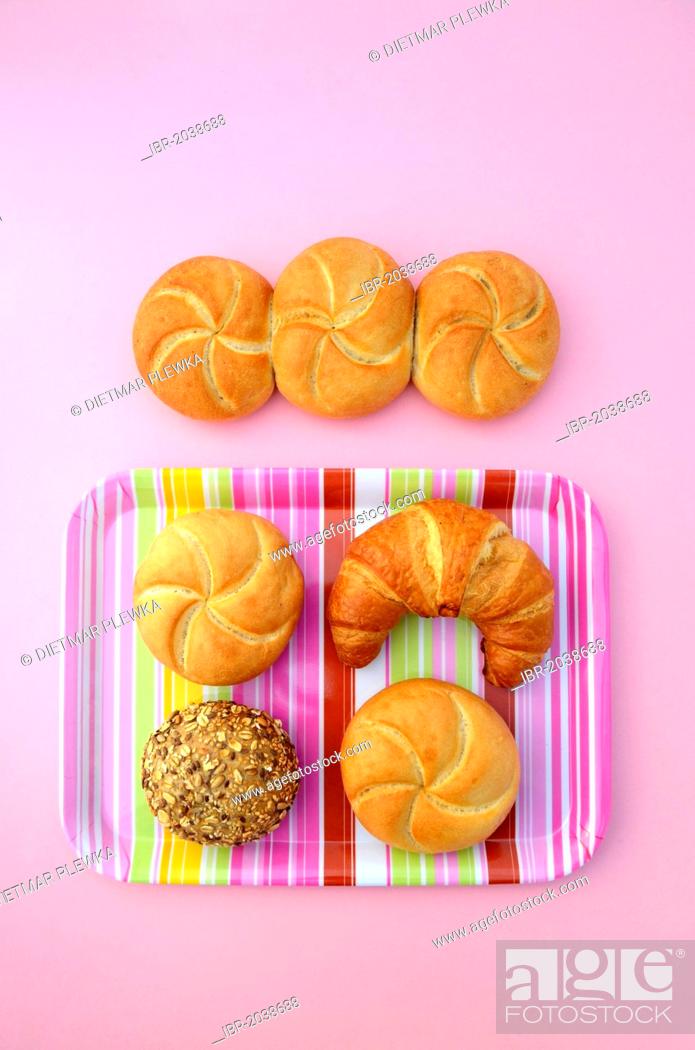Stock Photo: Bread rolls beside a croissant, a bread roll, a wholemeal roll and a multigrain roll on a striped, pink tray.