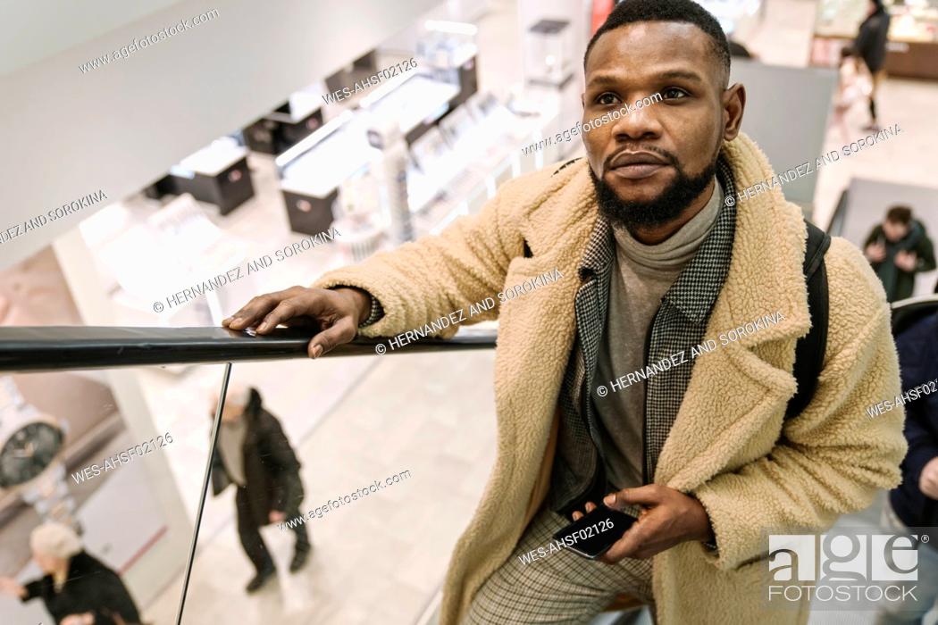 Stock Photo: Stylish man on escalator in shopping center holding smartphone.