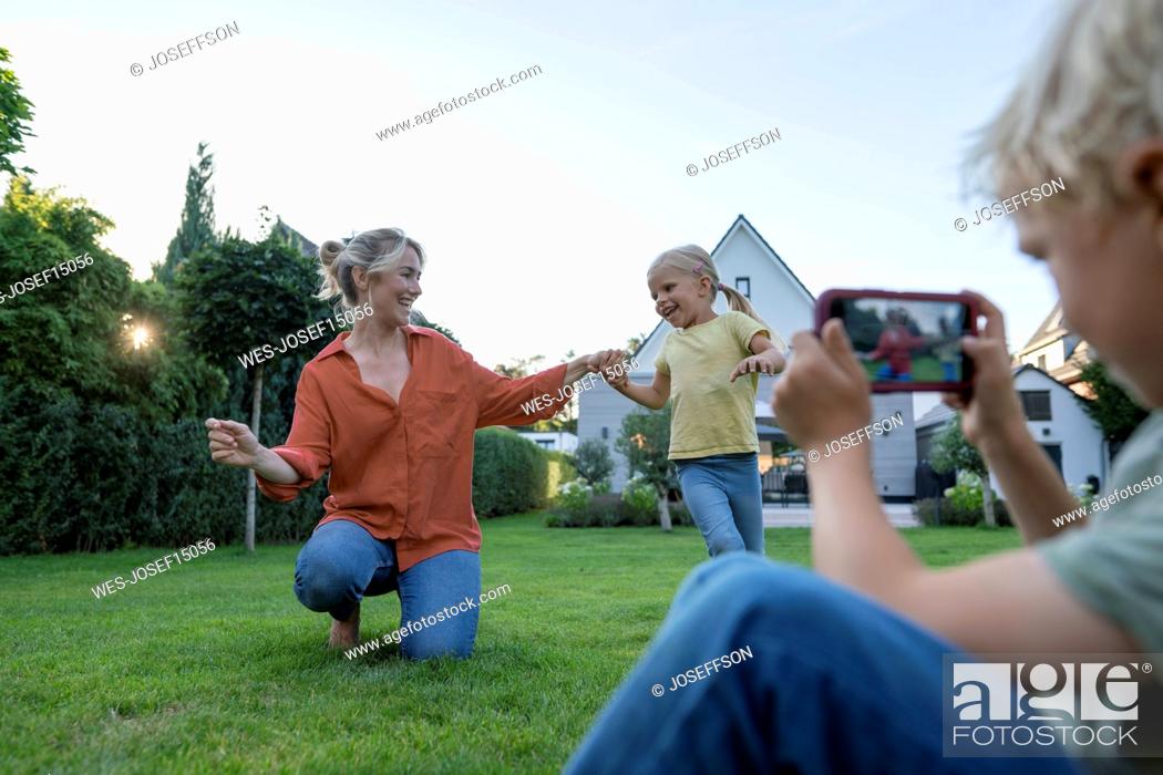 Photo de stock: Boy photographing mother dancing with girl through mobile phone in garden.
