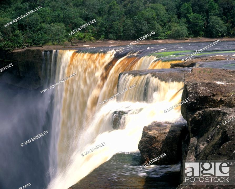 Stock Photo: Waterfall. Cascade of brown water over rock edge. Wide river. Foam rising. White water spray.Mist.