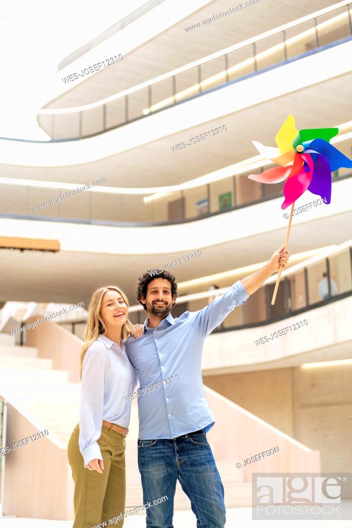 Stock Photo: Smiling businesswoman with colleague holding multi colored pinwheel toy in office lobby.