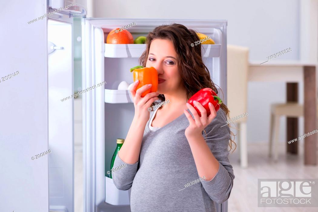 Imagen: Pregnant woman near fridge looking for food and snacks.