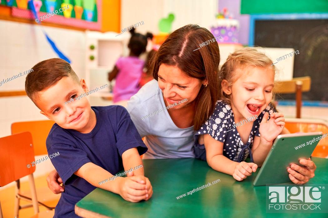 Stock Photo: Kindergärtnerin oder Erzieherin hat Spaß mit Kindern am Tablet Computer im Kindergarten.