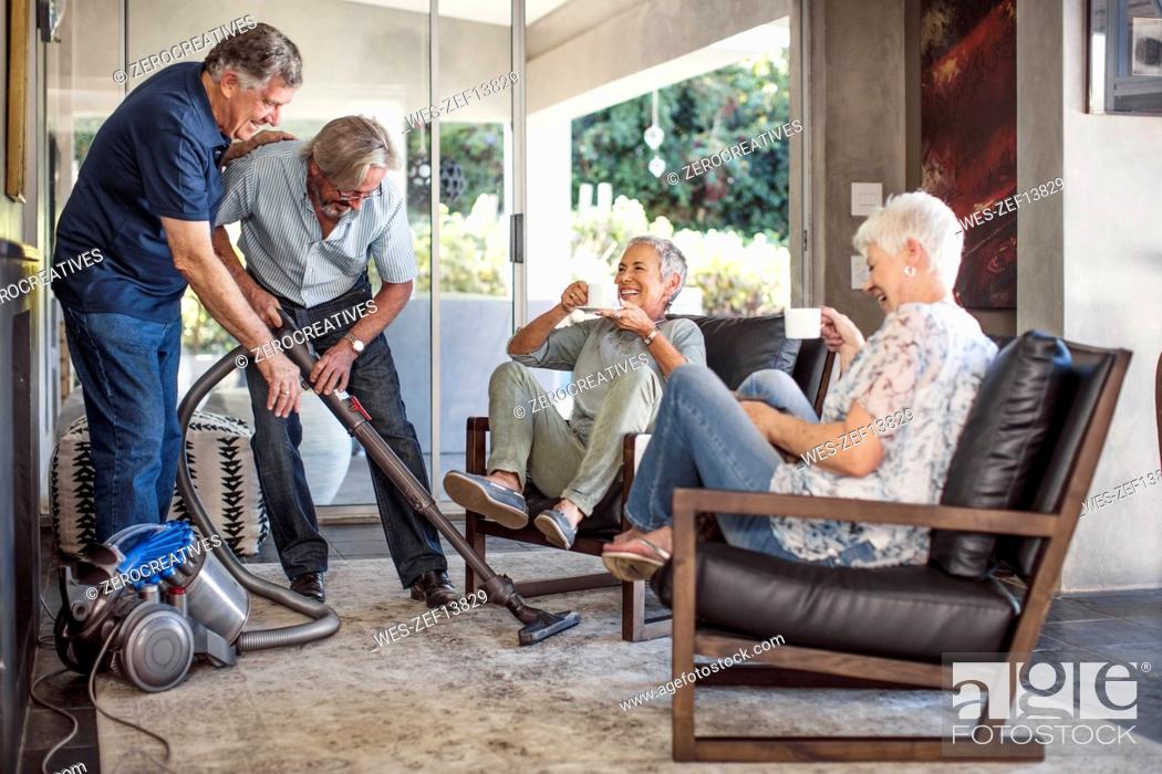Stock Photo: Two senior men vacuming house together while their wifes watching.