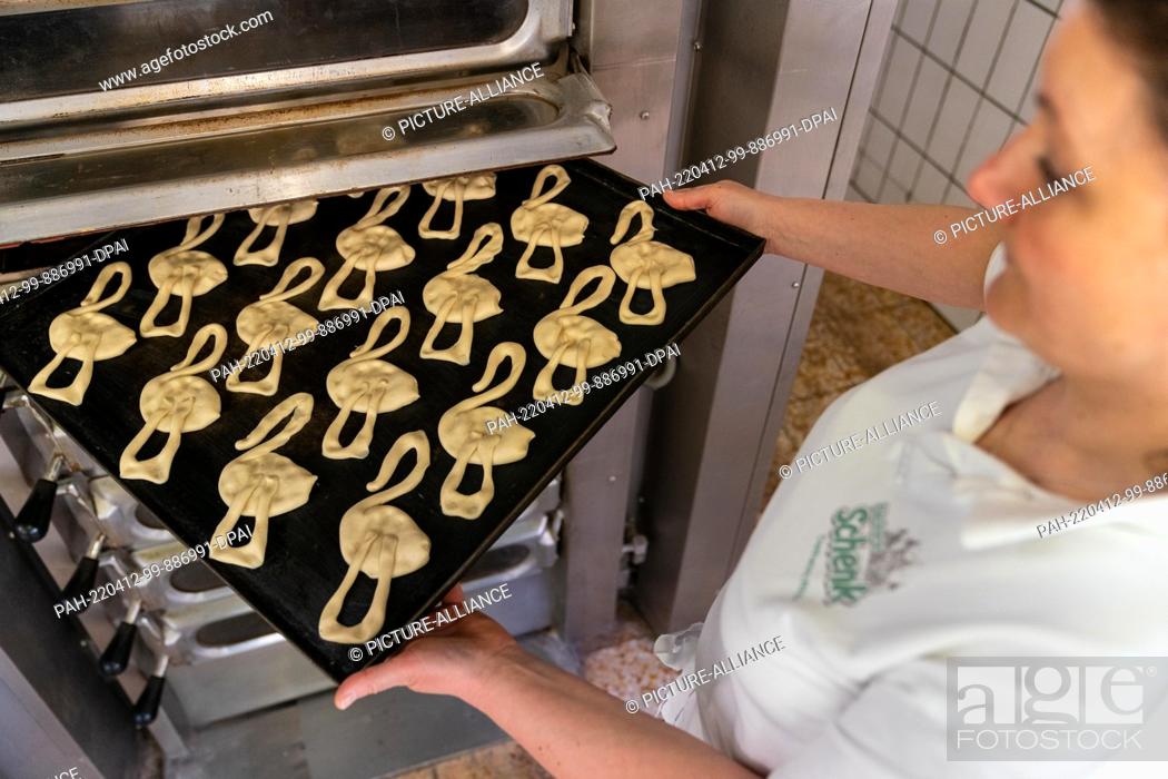 Photo de stock: PRODUCTION - 11 April 2022, Bavaria, Ostheim Vor Der Rhön: Master baker Juliane Witthauer puts a tray of Easter storks made of yeast dough in the oven.