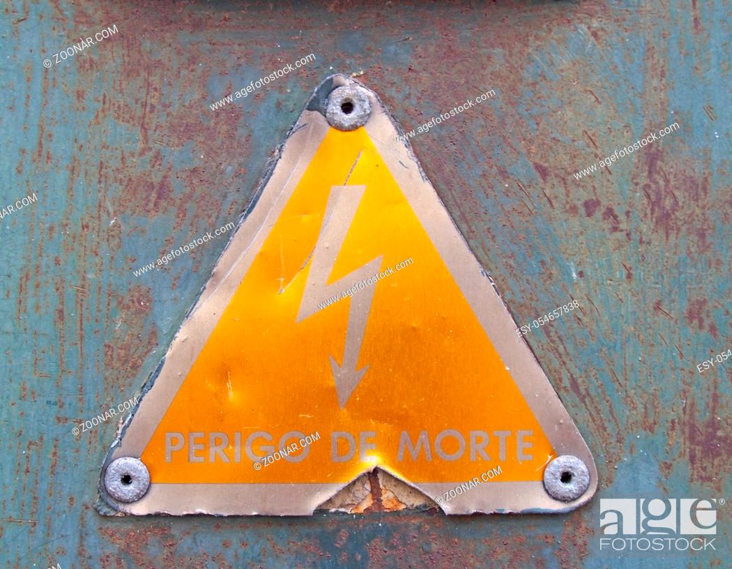 Imagen: an old metal triangular yellow Portuguese electricity safety sign with a lightning bold symbol reading perigo de morte - translation danger of death on a rusty.