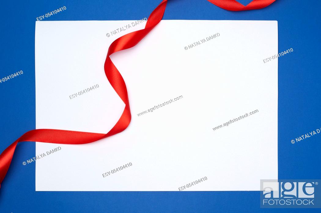 Imagen: empty white sheet of paper and red silk twisted ribbon on a blue background, place for test, holiday backdrop.
