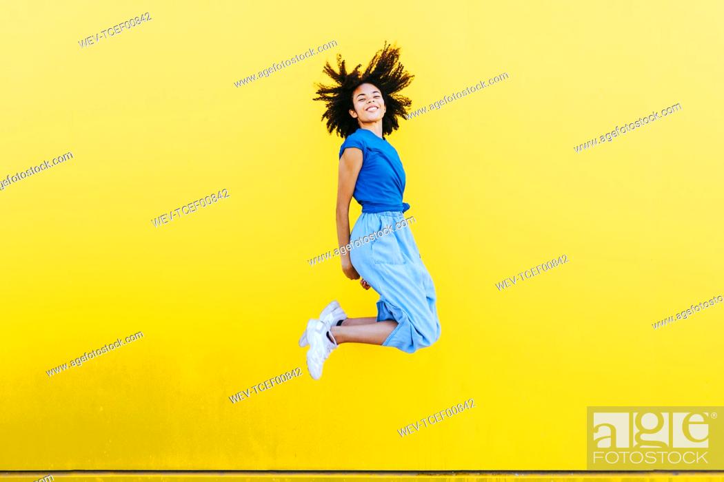 Stock Photo: Pretty woman jumping for joy in front of yellow wall.