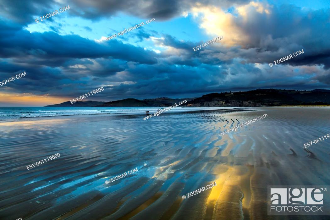 Stock Photo: Sunrise over the ocean. Low tide. Strips of sand and water left by the ocean tide. New Zealand, Pacific Coast. The concept of artistic photography.