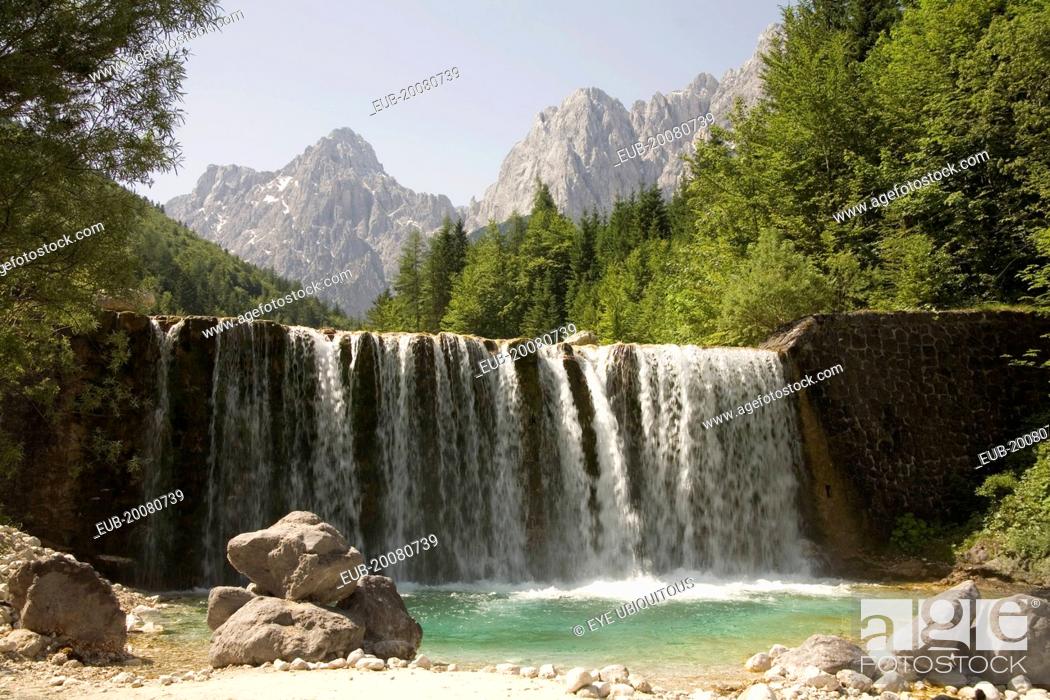 Stock Photo: A waterfall on Velika Pisnica with Mounts Razor and Prisank in the Julian Alps in the background. There is still snow lying on the mountain after a severe.