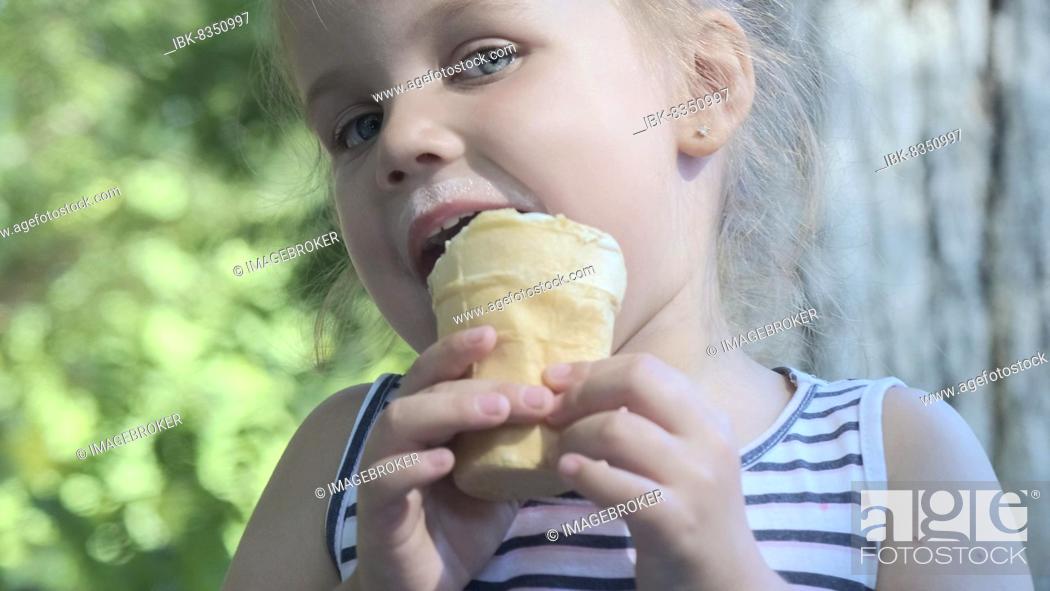 Stock Photo: Cute little girl eats ice cream outside. Close-up portrait of blonde girl sitting on park bench and eating icecream. Odessa, Ukraine, Europe.