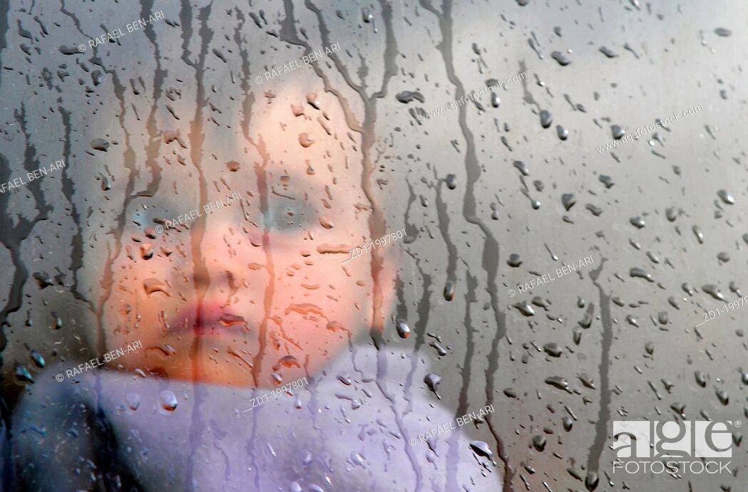 Stock Photo: A little baby watches the rain through the window.