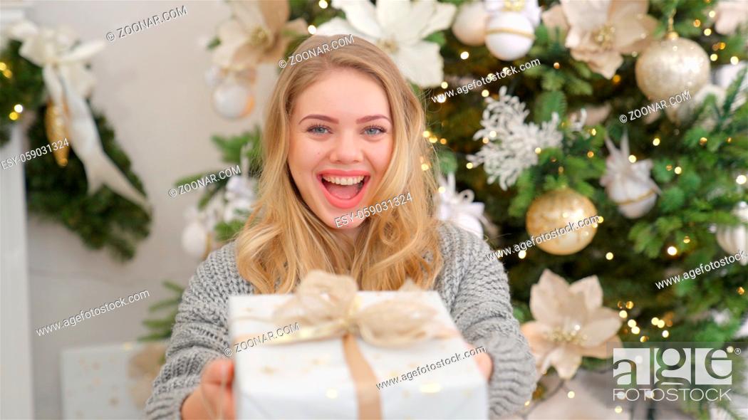 Imagen: Smiling and happy young woman with christmas present box near christmas tree. Xmas home concept.