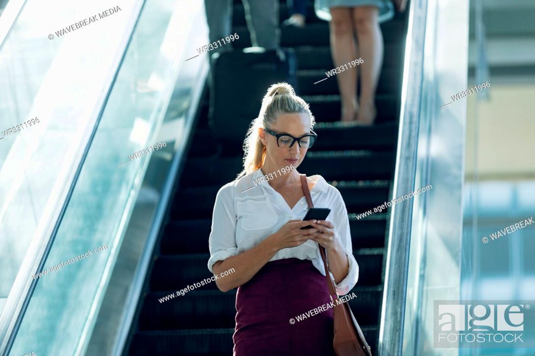 Stock Photo: Caucasian businesswoman looking at mobile phone while using escalators in modern office.