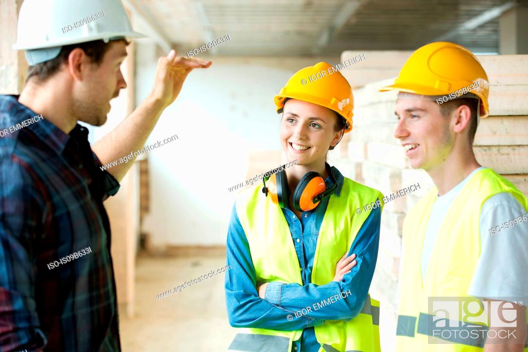 Stock Photo: Three people standing in constructions site, wearing hard hats, having discussion.