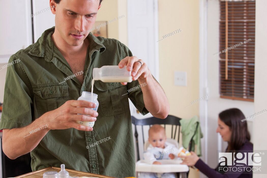 Photo de stock: Father preparing baby's formula and mother feeding baby.