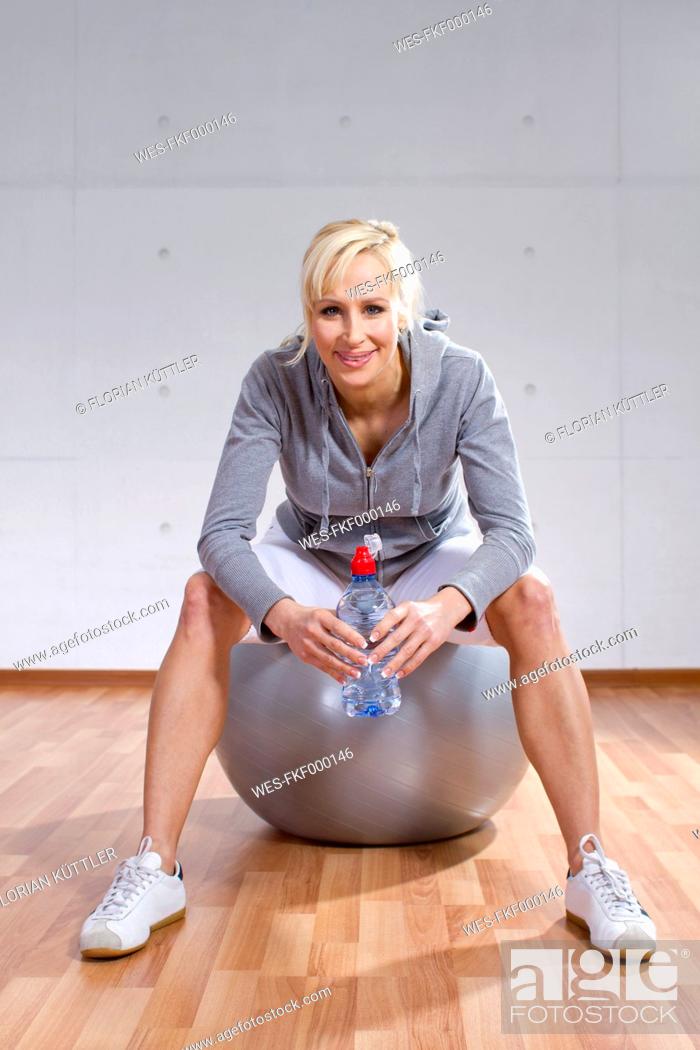 Stock Photo: Germany, Brandenburg, Portrait of woman sitting on fitness ball in gym, smiling.