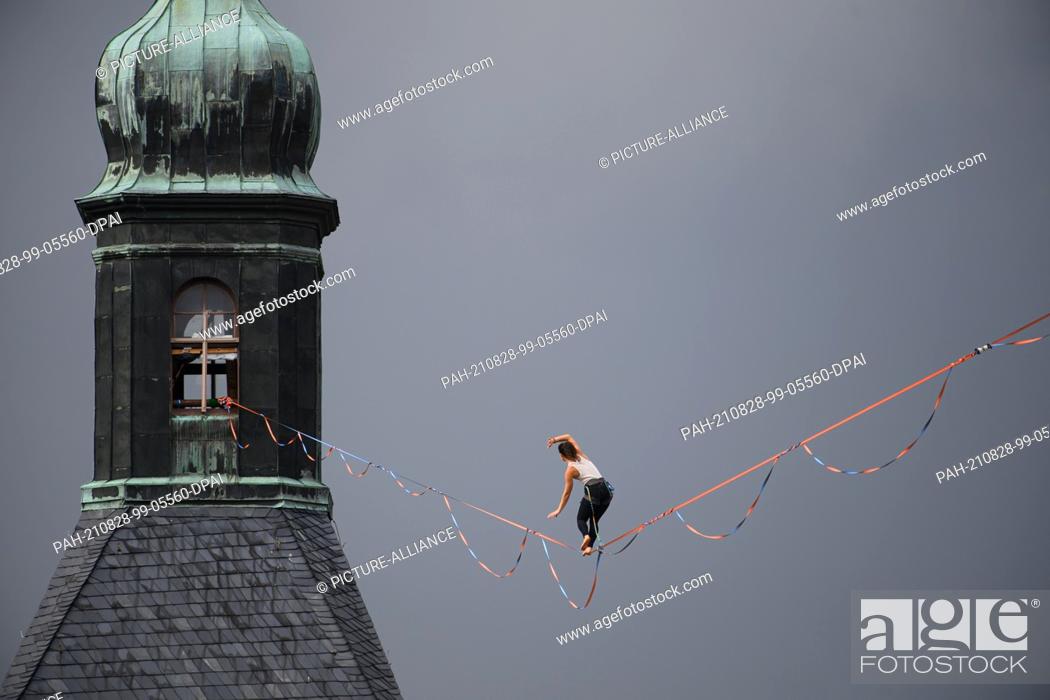 Stock Photo: 28 August 2021, Saxony, Hohnstein: A slackline runner balances on a rope between the castle and the town church of the town in Saxon Switzerland at the Highline.