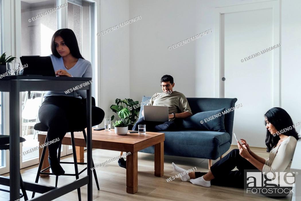Stock Photo: Two women and man studying through wireless technologies in living room.