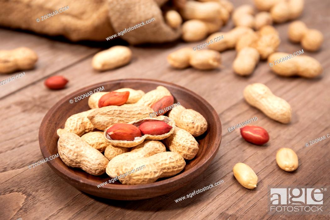 Stock Photo: Peanuts in bowl on rustic wooden table. Arachis hypogaea.