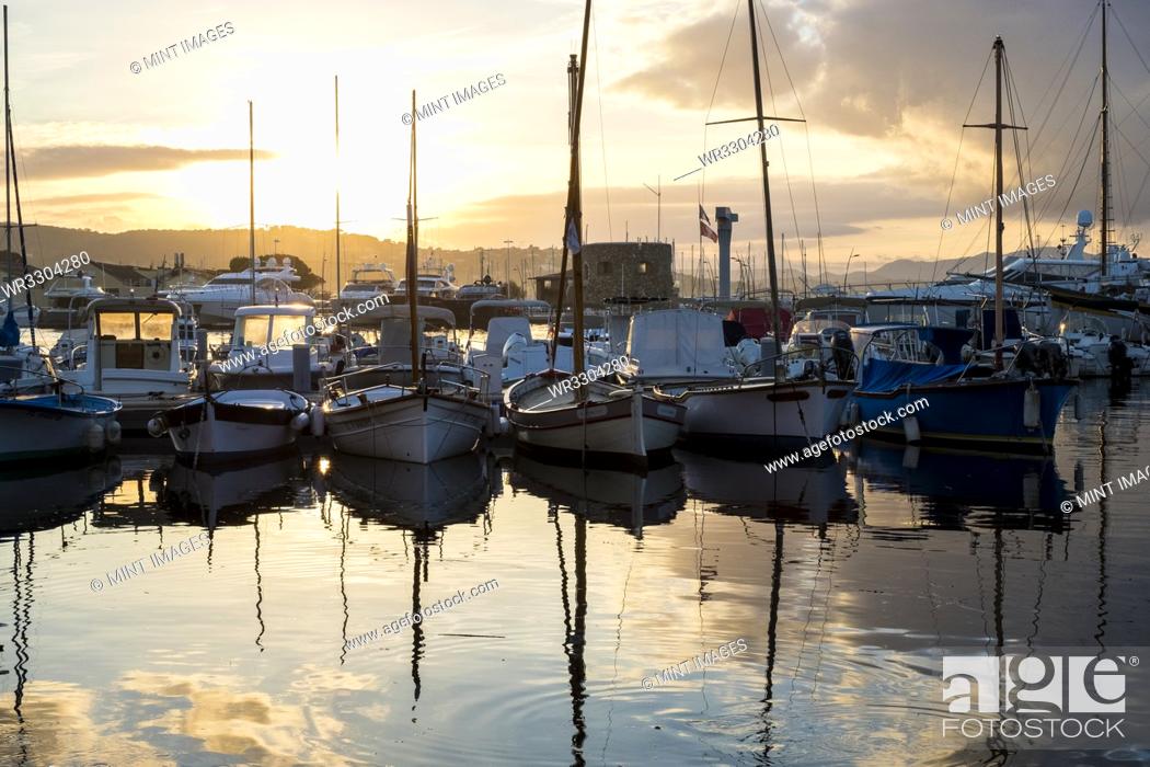 Stock Photo: Sailboats moored in harbour reflected in calm sea at sunset.