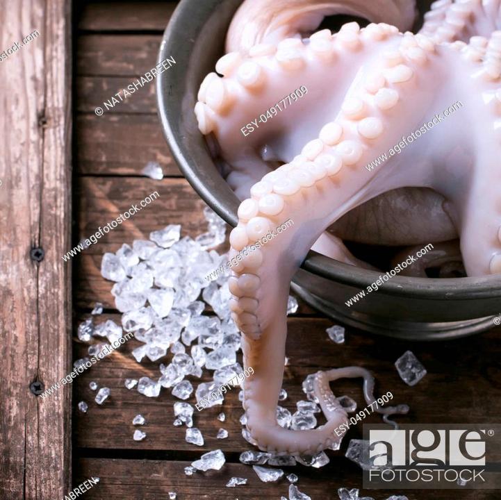 Stock Photo: Raw octopus on ice in vintage bowl over wooden background. Square image with selective focus.