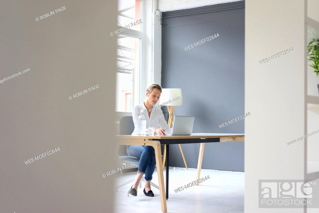 Stock Photo: Young businesswoman using laptop at desk in office.