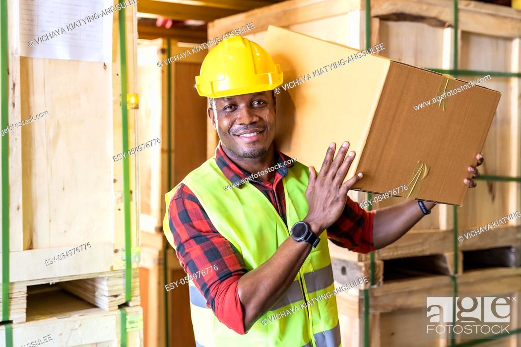 Stock Photo: Portrait of african black warehouse worker hold cardboard box packaging on his shoulder in large warehouse distribution center environment.