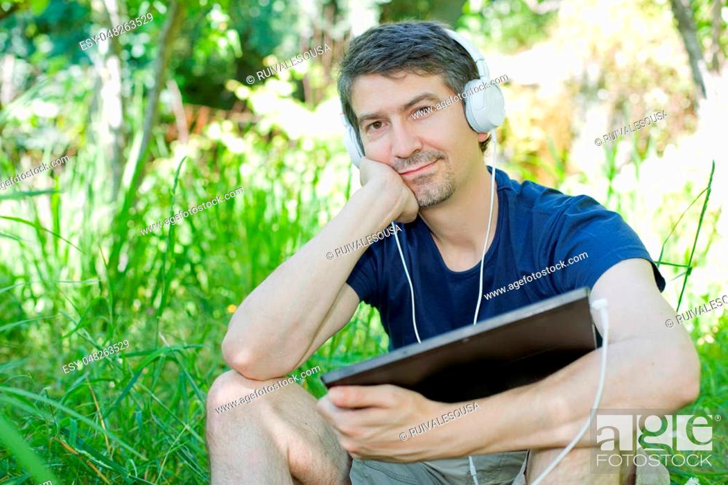 Stock Photo: young man relaxing with a tablet pc listening music with headphones on a the park, outdoor.