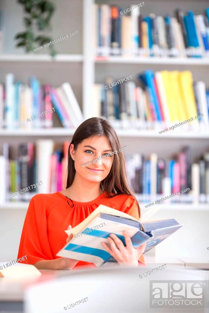 Stock Photo: Pretty, young college student looking for a book in the library, studying for her exam.