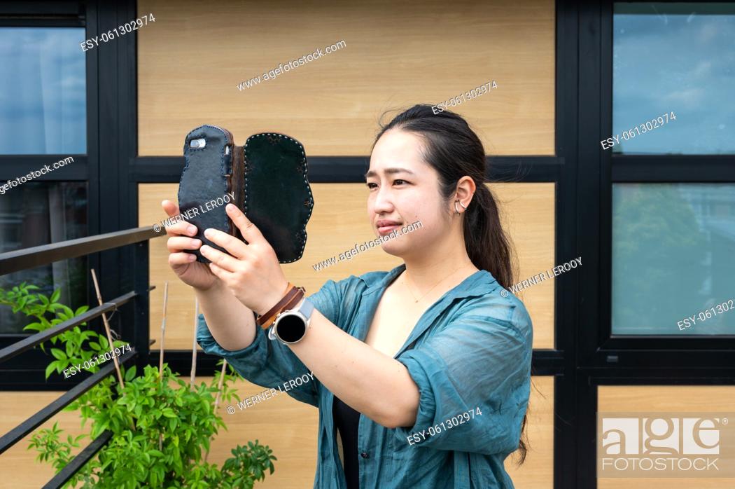 Stock Photo: Portrait of a 32 year old Japanese woman, taking a photo with her smartphone, Belgium.