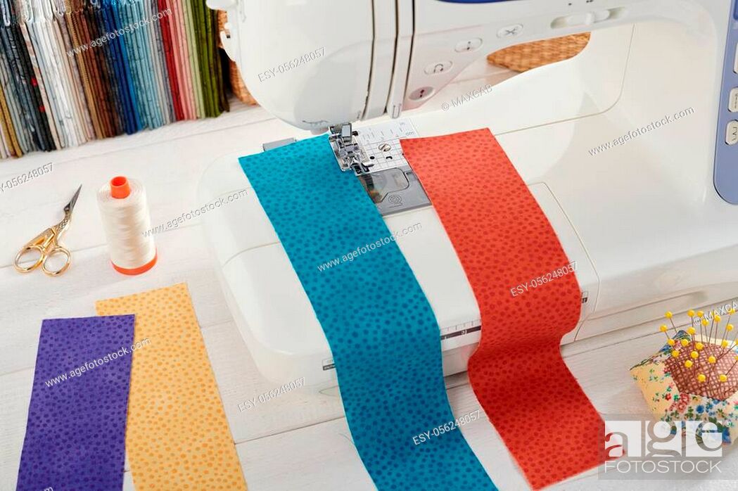 Stock Photo: Sewing machine with a strips of fabrics on the background of stack of colorful quilting fabrics, sewing accessories.