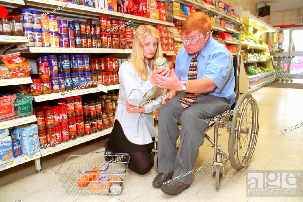Stock Photo: Man, who is wheelchair user, shopping in supermarket with assistance of teenage carer,.