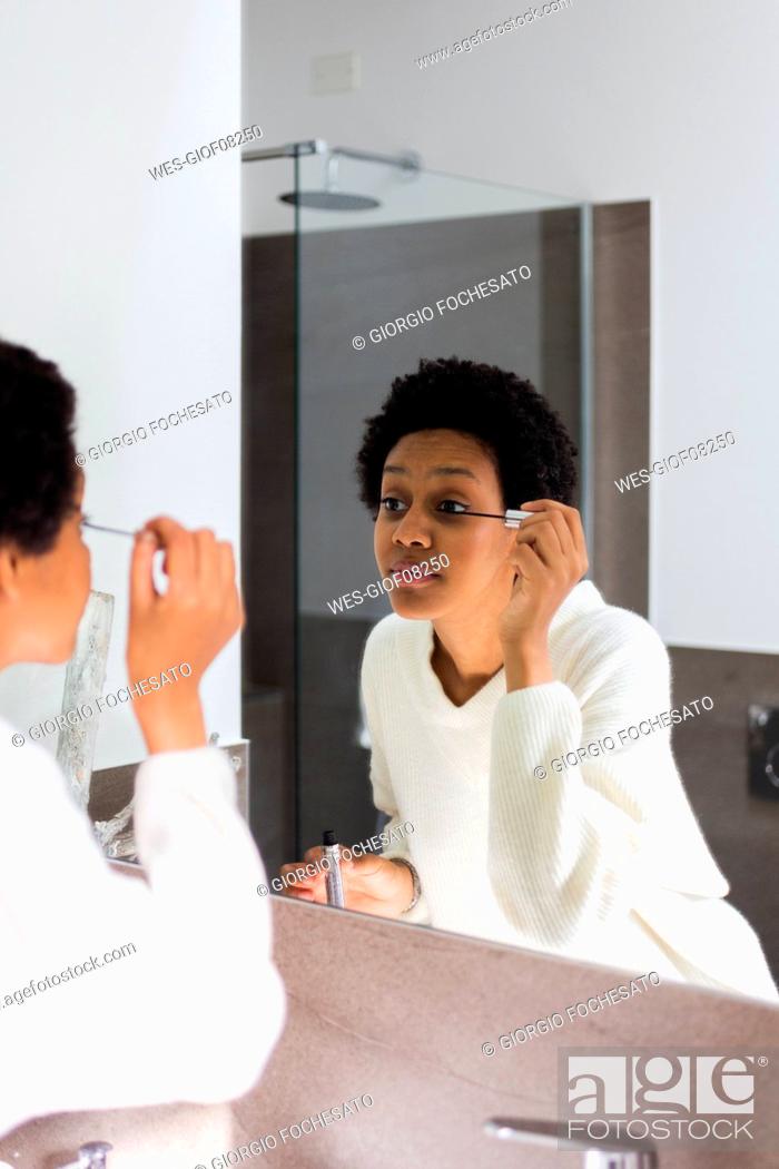 Stock Photo: Mirror image of young woman applying mascara.