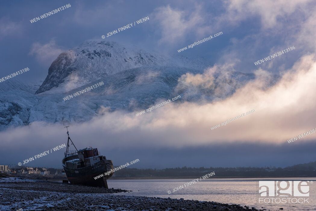 Stock Photo: A snow covered Ben Nevis emerges from a thick blanket of fog at sunrise with an old shipwreck at the side of Loch Eil, taken near Corpach and Fort William in.