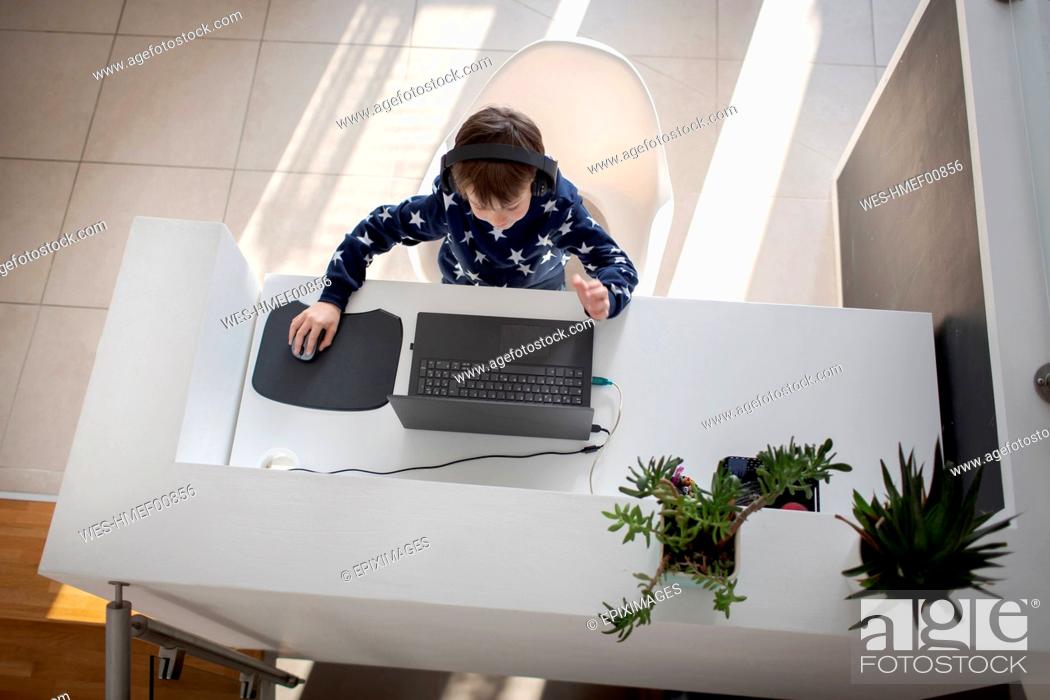 Stock Photo: Top view of boy sitting at desk at home wearing headphones and using laptop.