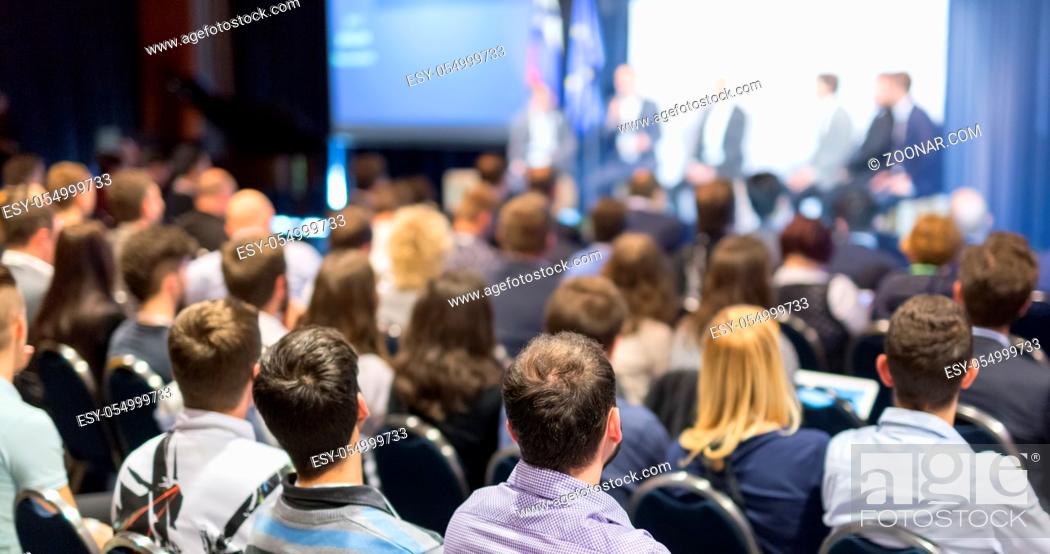 Stock Photo: Round table discussion at business and entrepreneurship symposium. Audience in conference hall. Lens focus on unrecognized participant in rear of audience.