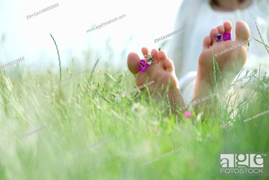 Stock Photo: Barefoot young woman sitting in grass with wildflowers between toes, cropped.