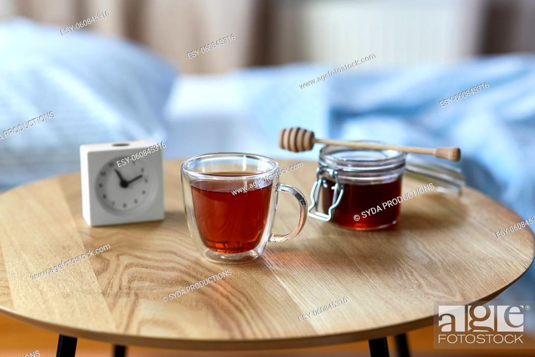 Stock Photo: cup of tea, honey and alarm clock on table.
