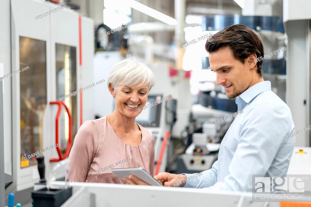 Stock Photo: Smiling businessman and senior woman with tablet talking in a factory.