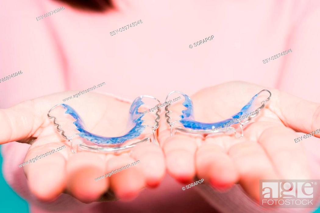 Stock Photo: Close up hands of young woman holding silicone orthodontic retainers for teeth, Teeth retaining tools after removable braces, isolated blue background.