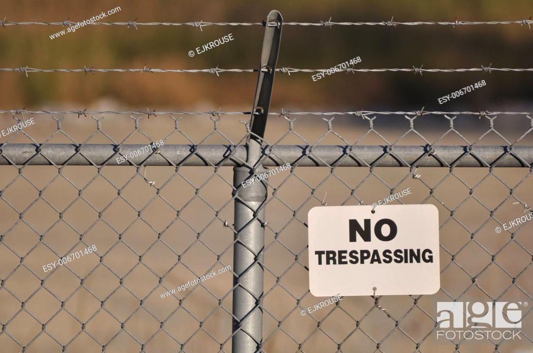 Stock Photo: No trespassing sign hanging on a menacing barbed wire fence.
