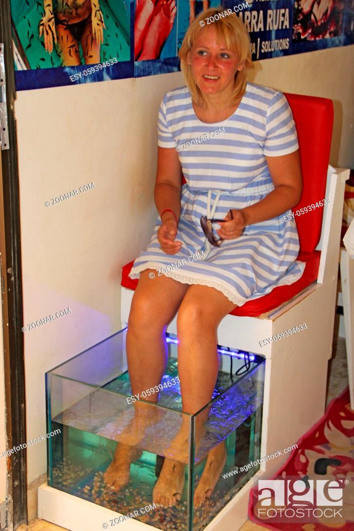 Photo de stock: Young woman receiving massage with small fishes. Peeling with fish. Girl enjoying medicinal procedure. Foot massage with fish in aquarium closeup.