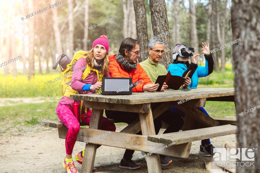 Stock Photo: Mature man with solar panel sitting by friends at picnic table in forest.